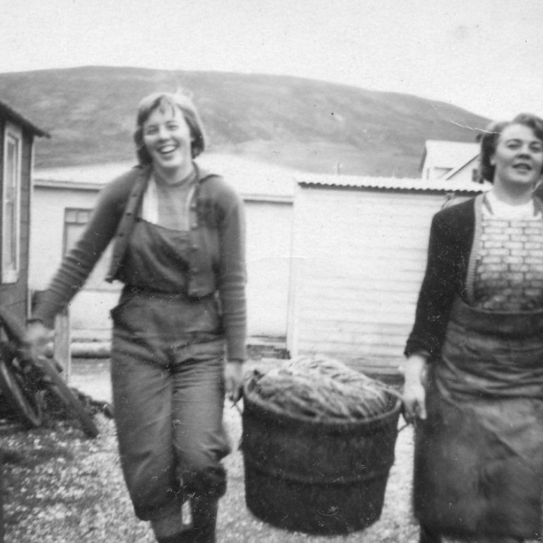 Inga Stína Stefánsdóttir og Hildigunnur Jónsdóttir með línubalann á milli sín. Að baki þeirra sést í Esso-skúrinn og Gömlu búðina